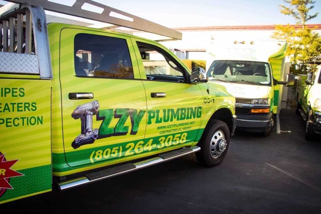 Izzy Plumbing service trucks parked, featuring bright yellow and green branding, emphasizing emergency plumbing services and sewer line inspections in San Luis Obispo.