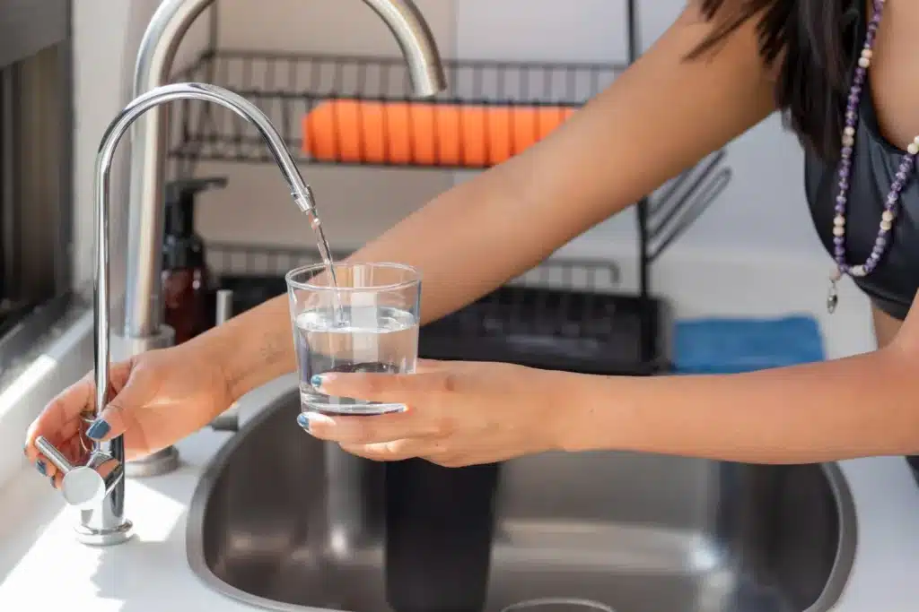 Woman pouring clear water into a glass from a modern kitchen faucet, emphasizing proper plumbing and maintenance in residential settings.