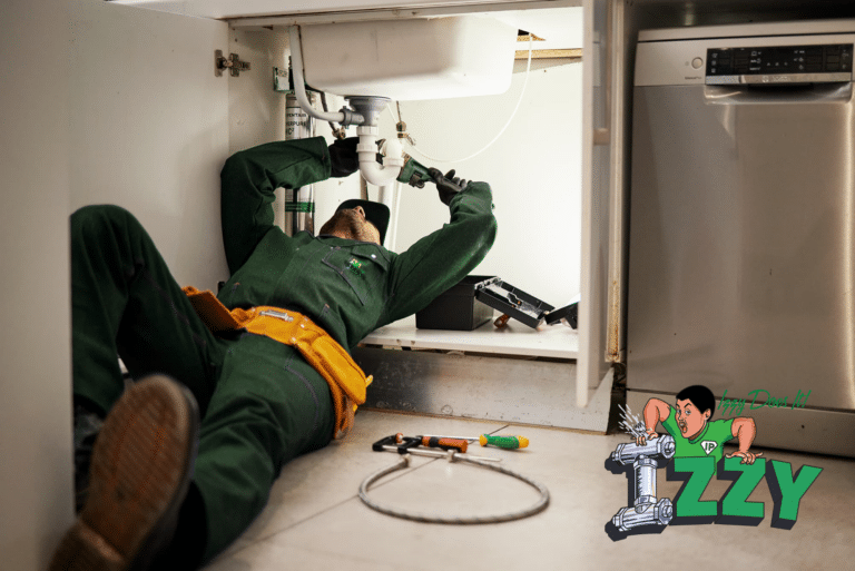 Plumber in green uniform performing emergency drain cleaning under a kitchen sink, featuring tools and Izzy Plumbing logo.